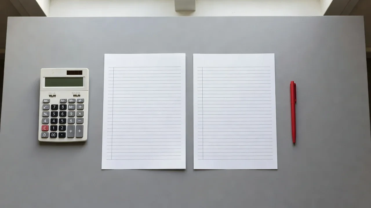 Desk with a calculator, printed statistics sheets and a red pen circling numbers, top-down view