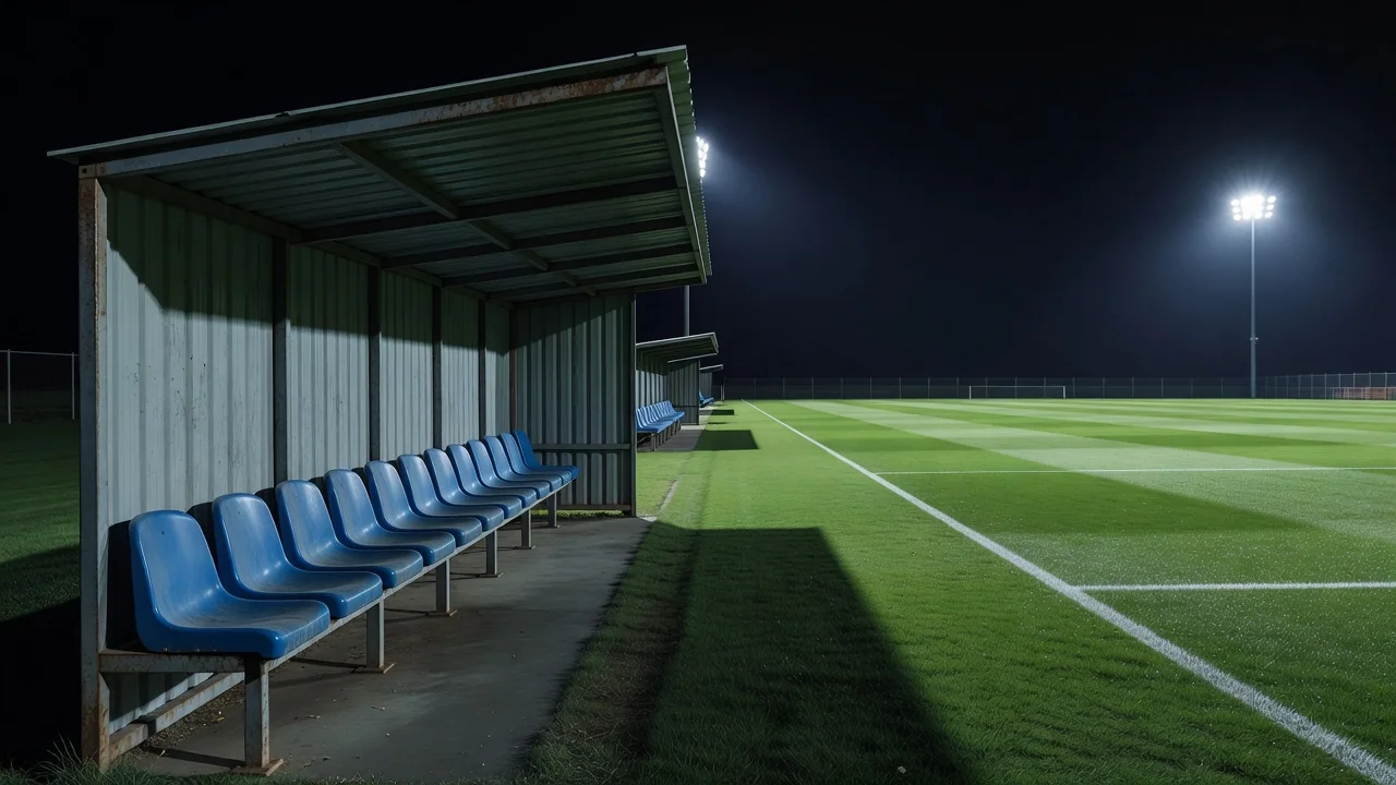 Empty substitutes dugout seats beside a floodlit football pitch at night